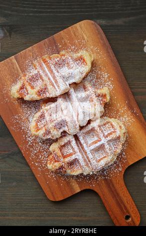 Frisch gebackene Croffles, bestreut mit Puderzucker auf Holzbrotbrett Stockfoto