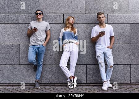 Fashion Portrait von drei besten Freunden posiert auf der Straße, trägt stilvolle Outfit und Jeans gegen graue Wand. Stockfoto