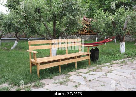 Eine Hängematte zwischen zwei Bäumen in einem üppigen grasbewachsenen Garten mit einer Holzbank im Hintergrund Stockfoto