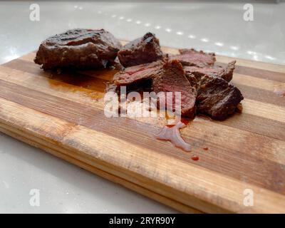 Köstliches und saftiges Rindersteak in Scheiben geschnitten auf einem Holzschneidebrett mit Streifen. Stockfoto