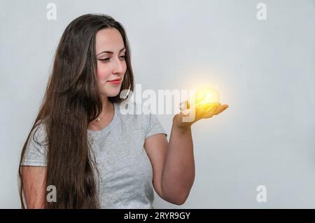 Glühbirne leuchtet in der Hand einer dunkelhaarigen, süßen Frau. Energieeinsparung. Neue Technologien. Stockfoto
