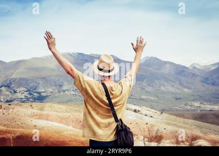 Männlicher Tourist mit offenen Händen steht auf einem Berg und blickt auf eine Bergkette Stockfoto