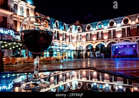 Glas Rotwein auf einem Tisch mit Reflexion in einem Café auf einer leeren Piazza in Batumi Georgia Stockfoto