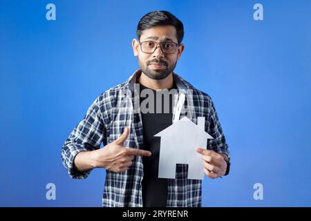 Indischer Mann zeigt das Konzept des Hauskredits, isoliert auf blauem Hintergrund. Stockfoto