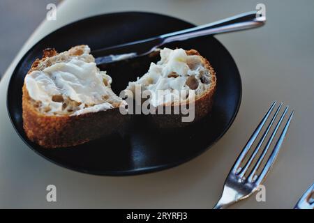 Bennelong Sauerteig mit Zuchtbutter, ein Stück gebackenes Brot im Restaurant mit Butter auf einem dunklen Teller mit einem Buttermesser und einer Gabel. Stockfoto