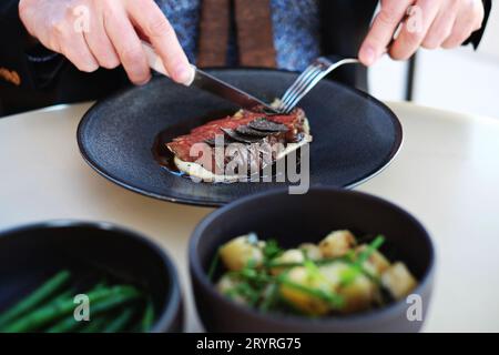 Zwei Hände, Messer und Gabel mit einer Portion Blackmore Wagyu (9+) mit WA-Trüffel, Madeira Jus - feine Küche im Bennelong Restaurant, Sydney Opera House Stockfoto