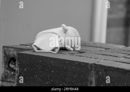 Ein schwarz-weißes Bild eines kleinen Kinderschuhs auf einer Ziegelmauer in einer Stadtstraße Stockfoto