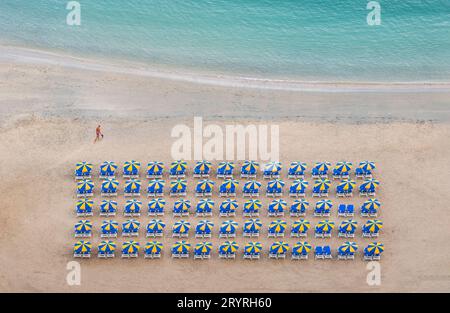 Liegestühle sind ordentlich in Reihen unter bunten Sonnenschirmen in der Nähe des Meeres an einem sonnigen Strand in Amadores, Gran Canaria, Spanien, angeordnet. Stockfoto