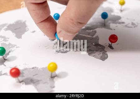 Nahaufnahme der menschlichen Hand, die auf der Weltkarte feststeckt. Konzept für Reiseziele Stockfoto