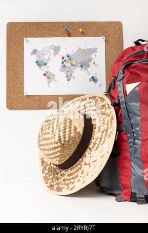 Reiseziel planen Konzept. Korkboard mit Weltkarte und Pins an der Wand, Rucksack und Sommerhut Stockfoto