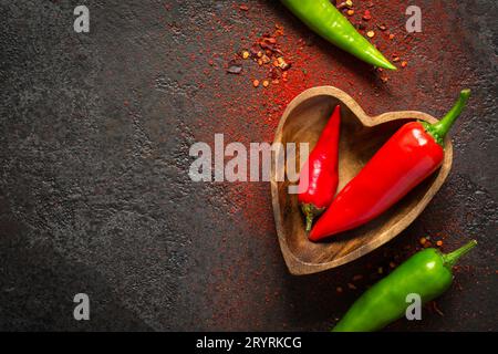 Dunkler Hintergrund von Gewürznahrung. Rote und grüne Pfeffer in einer Holzschale Stockfoto