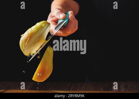 Frau schneidet eine Birne in zwei Hälften mit einem Messer in der Luft, das Wasser verschüttet, Spritzeffekt, isoliert auf schwarzem Hintergrund. Hochgeschwindigkeitsfotografie. Stockfoto