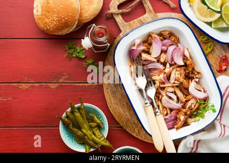 Gezapftes bbq-Hühnchen mit gebackenen Zwiebeln auf Servierplatte, bbq-Mais, Gurken, Chilischoten und Brötchen für Hot Dogs und Burger, Tomatensauce. Traditionell Stockfoto