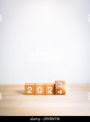 2024 Frohes neues Jahr mit dem Wechsel zu neuen Zeitkonzepten. Drehen der Kalendernummern für 2023 bis 2024 Jahre auf Holzwürfelblöcken, die auf Holztisch und isoliert sind Stockfoto