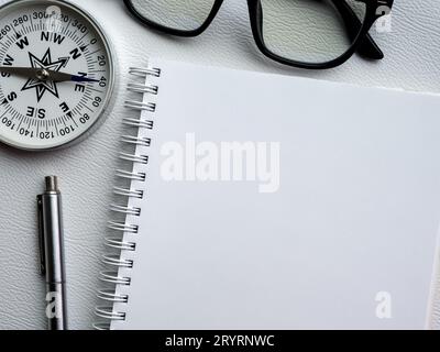 Mockup-Bereich auf neuer Seite auf Spiralnotizbuch. Weiße leere Vorlage auf Tagebuchnotizblock mit Stift, Kompass und schwarzer Brille. Nahaufnahme-Papier zum Zeichnen, Verkleinern usw. Stockfoto