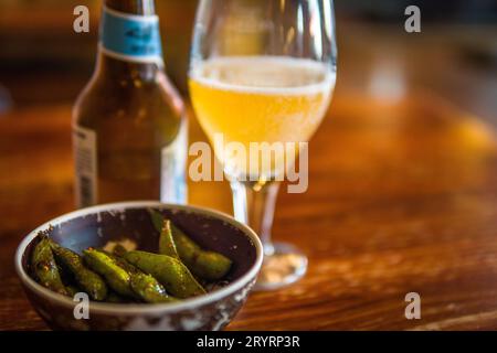 Deliciou Edamame Bean Snack auf Holztisch mit japanischem Bier im Hintergrund. Traditionelles japanisches Taverne-Konzept Stockfoto