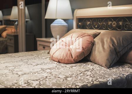 Klassisches Bett mit Samtkissen auf geblümtem Bettüberwurf. Fragment der Innenausstattung des Schlafzimmers im klassischen Stil, Abendbeleuchtung Stockfoto