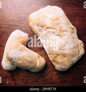 Ein frisch geschnittenes Brot, das neben zwei kleineren Brötchen auf einem Holztisch steht Stockfoto