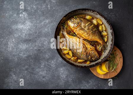 Gebackene Dorade oder Dorada mit Zwiebeln und Kräutern in der Pan auf dunklem Hintergrund Stockfoto