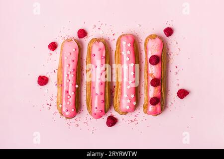 Kreatives Layout aus Eclairs mit rosa Glasur auf rosa Hintergrund. Einfarbiges Lebensmittelkonzept Stockfoto