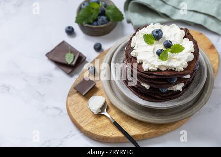 Wir feiern den Pfannkuchentag. Köstliche hausgemachte amerikanische Bananen Schokoladenpfannkuchen mit Heidelbeeren und Ricotta auf einem Marmortisch Stockfoto