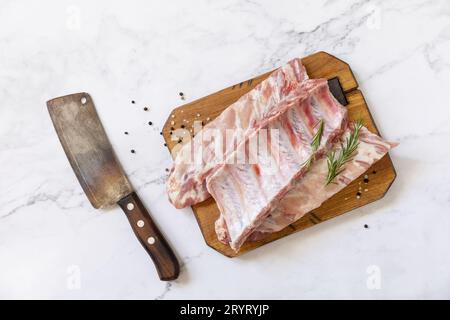 Rohes Kalbsbriketts Fleisch mit Rosmarin und Gewürzen auf kurzen Rippen zum Kochen auf Marmorplatte. Draufsicht, flach liegend. Stockfoto