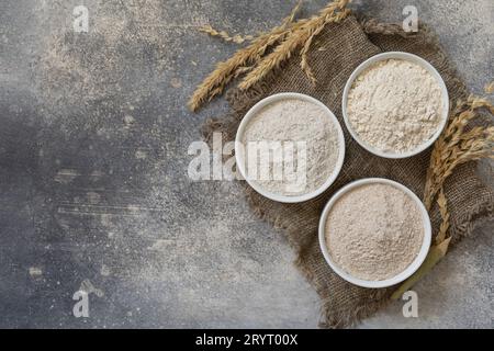 Lebensmittel und Backzutaten. Weizenmehl grob von Vollkornkörnern, Weizenkleie und Weizenmehl über grauem Steinhintergrund. T Stockfoto