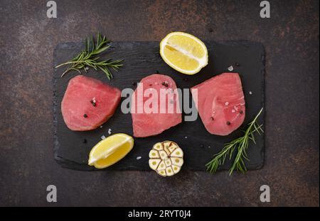 Meeresfrüchte. Rohe saftige Thunfischsteaks mit Gewürzen und Rosmarin auf einem Steintisch. Blick von oben. Stockfoto