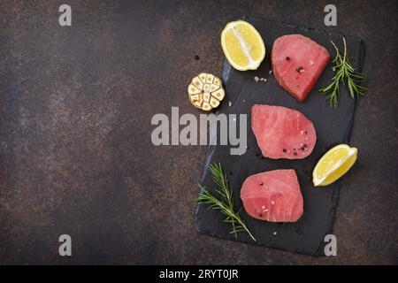 Meeresfrüchte. Rohe saftige Thunfischsteaks mit Gewürzen und Rosmarin auf einem Steintisch. Blick von oben. Speicherplatz kopieren. Stockfoto