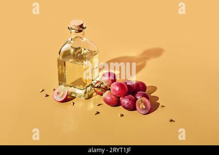 Traubenkernöl in Flasche und Traubenbündel auf gelbem Hintergrund und trendigen Schatten. Lebensmittelabfälle wiederverwenden Stockfoto