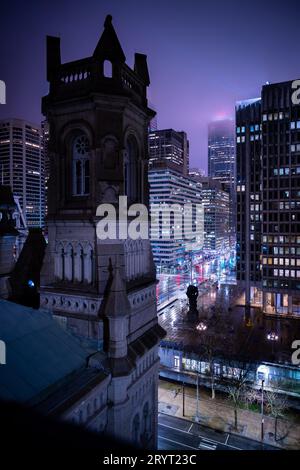 Eine städtische Straßenszene mit beleuchteten Gebäuden im Hintergrund und einem Uhrturm in der Mitte Stockfoto