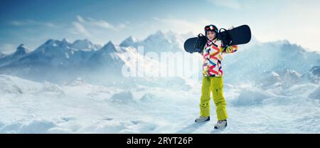 Junge Frau in Sportbekleidung, die mit Snowboard über schneebedeckten Bergen im Hintergrund steht. Winterurlaub Stockfoto