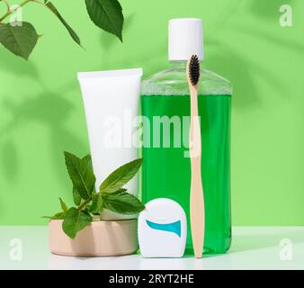 Erfrischende Mundspülung in einer durchsichtigen Plastikflasche und Zahnseide, weiße Tube auf grünem Hintergrund Stockfoto