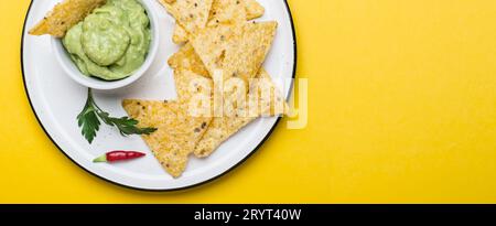 Traditionelle lateinamerikanische Guacamole mit Corn Chips Nachos auf gelbem Hintergrund. Bannerformat Stockfoto