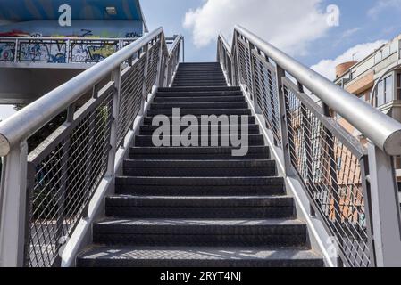 Eine Treppe führt zu einem Metallsteg in einem Stadtpark neben einer Ringstraße Stockfoto