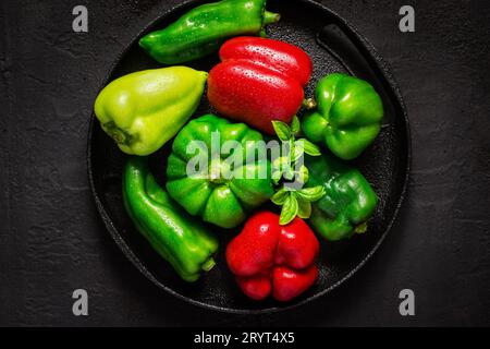 Verschiedene rote und grüne Paprika mit Wassertropfen auf schwarzem Hintergrund Stockfoto