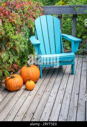 Leerer Adirondack-Stuhl mit Kürbissen auf einer hölzernen Terrasse im Hinterhof, Herbstlandschaft in Colorado Stockfoto
