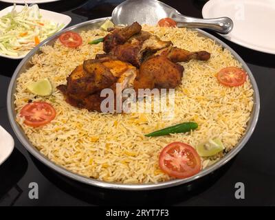 Hühnchen Biryani serviert auf einem großen Stahlteller und garniert mit Tomatenscheiben, grünem Chili und Zitronenscheiben. Stockfoto