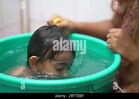 Ein 2-jähriger indischer Junge, der in einer grünen Badewanne badet. Stockfoto