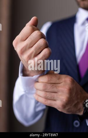 Ein junger Mann, der einen maßgeschneiderten Anzug und eine Krawatte trägt und seine Armbanduhr in einer professionellen Umgebung anpasst Stockfoto