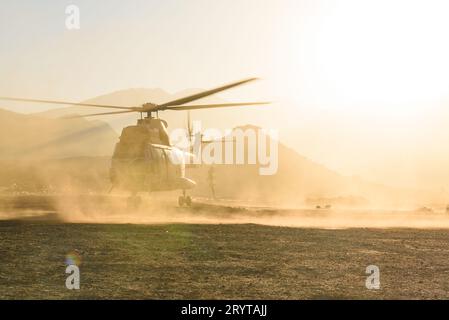 Ein Militärhubschrauber fliegt und landet in der Wüste bei Sonnenuntergang in einer Staubwolke. Luftwaffe Stockfoto