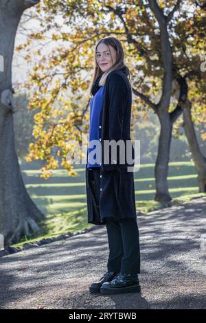 Eine Frau in gemütlicher Herbstkleidung steht inmitten des bunten Laubs großer Bäume, die mit Herbstlaub geschmückt sind Stockfoto