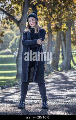 Eine Frau in gemütlicher Herbstkleidung steht inmitten des bunten Laubs großer Bäume, die mit Herbstlaub geschmückt sind Stockfoto