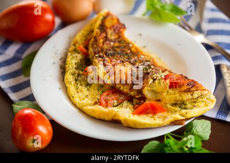 Gefülltes Omelett mit Tomaten auf hellem Holzgrund. Gesunde Ernährung zum Frühstück. Stockfoto