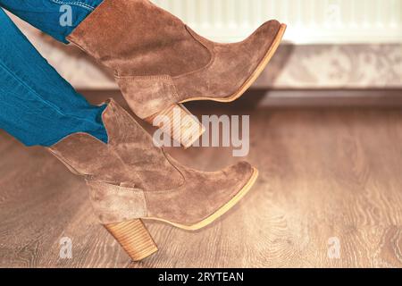 Nahaufnahme. Wildlederstiefel für Damen. Braune Damenschuhe. Beim Mädchen werden warme Stiefel auf die Beine gestellt. Schuhanpassung.Konzept des Kaufens, des Versuchs an Schuhen und Stiefeln. Stockfoto