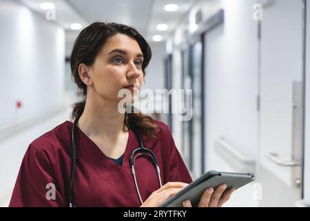 Kaukasische Ärztin mit Peelings und Stethoskop, mit Tablette im Flur im Krankenhaus Stockfoto