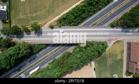 Blick aus der Vogelperspektive auf die Straße mit Brücke über eine Autobahn und Wald und Felder daneben an einem sonnigen Sommertag. Autobahn in Belgien. Stockfoto