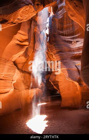 Mittag in einem rot-Orange Antelope Canyon. Ein dünner Strahl des Tageslichtes leuchtet auf dem sandigen Boden des Canyons Stockfoto