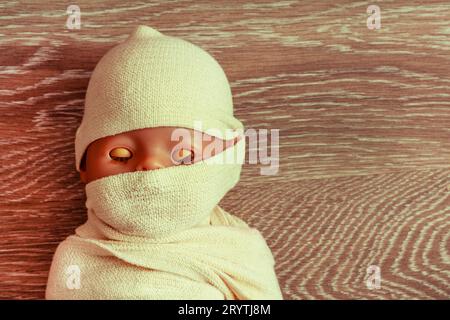 Die Puppe das Baby wird mit Stoff umwickelt. Der Körper des Kindes ist in ein Schutztuch gehüllt. Das Konzept der muslimische Tote. Eine Mumie auf einem Hintergrund. clos Stockfoto