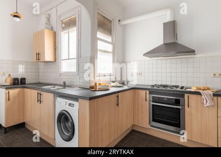 Stilvolle Küche mit Einbaugeräten, Ofen und Waschmaschine mit Dunstabzug und weißen Fliesen in einem modernen Apartment. Konzept eines 5-Sterne-Hotels Stockfoto